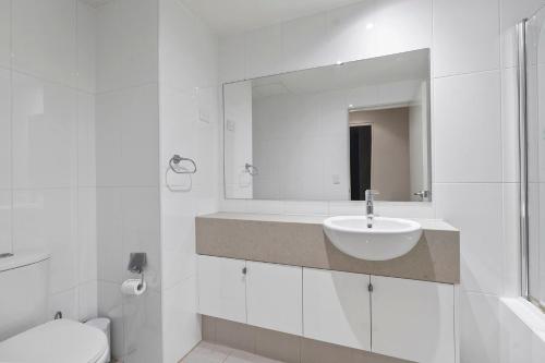 Baño blanco con lavabo y espejo en Coast on Coral Luxury Apartment Unit 15, en The Entrance
