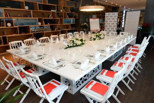 a long white table with white chairs and plates and flowers at TAV Airport Hotel Izmir in Izmir
