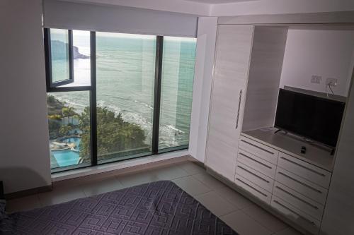 a room with a large window with a television and a bathroom at Departamento Suite frente al mar Poseidon Manta in Manta