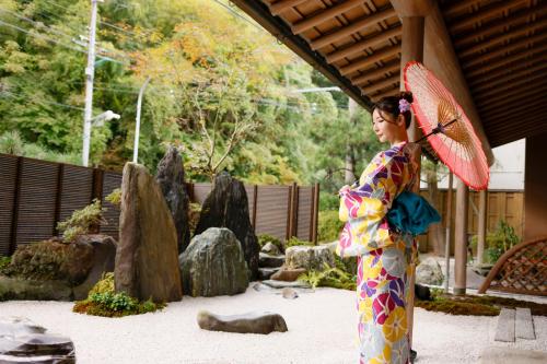 a woman in a kimono holding a red umbrella at Kawaguchiya Kinosaki Riverside Hotel in Toyooka