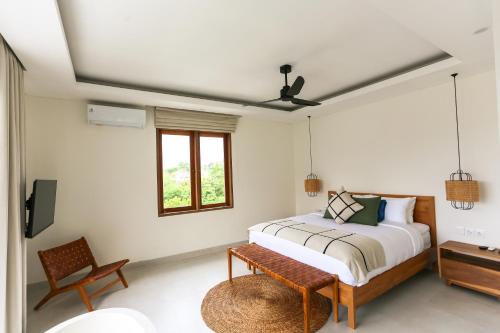 a bedroom with a bed and a chair and a window at Shoreline Villas Bingin in Uluwatu