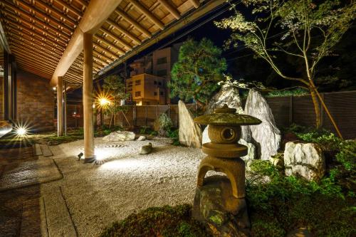 a japanese garden with a stone lantern in front of a building at Kawaguchiya Kinosaki Riverside Hotel in Toyooka