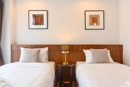 two beds in a room with two lamps and pictures on the wall at Be Phrasingh Hotel Chiang Mai in Chiang Mai