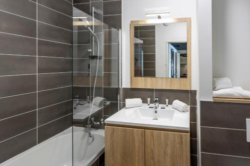 a bathroom with a sink and a mirror and a tub at Nemea Appart Hotel Riviera Nice Aéroport in Nice