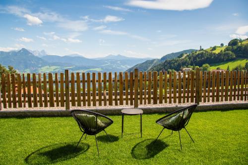 zwei Stühle und ein Tisch im Gras mit einem Zaun in der Unterkunft Haidgerberhof - apartments & homemade food in Lengstein