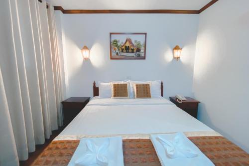 a bedroom with a large white bed with two tables at khampiane hotel in Ban Nongdouang