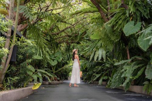 a woman in a white dress walking down a path in a forest at The Gems Mining Pool Villas Pattaya in Nong Prue