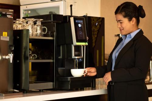 a woman holding a cup of coffee in front of a counter at Mila Hotel in Kathmandu