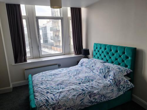 sypialnia z łóżkiem z niebieskim zagłówkiem i oknem w obiekcie Luxury 2 Bedroom, and 2 Bathroom Apartment w Cardiff