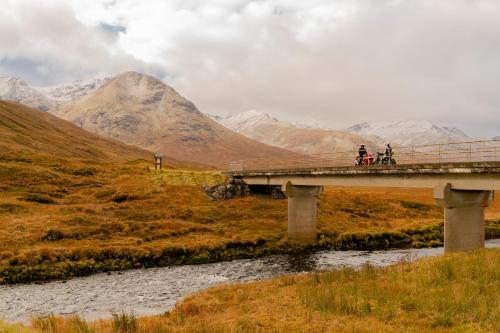 two people riding bikes on a bridge over a river at The Cluanie Inn in Glenmoriston