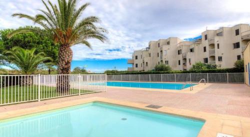 une piscine avec un palmier et quelques bâtiments dans l'établissement Les Fregates - Appart 4 pers proche plage et piscine, à Saint-Cyprien