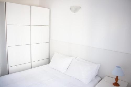 a white bed with white pillows and a lamp at Apartamentos Central in Quarteira