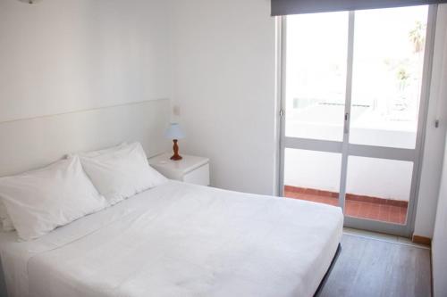 a white bed in a room with a large window at Apartamentos Central in Quarteira