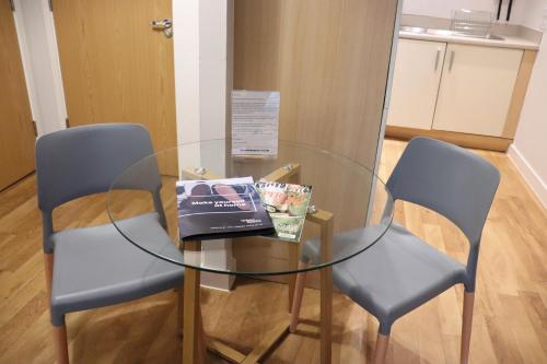 a glass table with two chairs and a book on it at Quayside Apartments in Cardiff