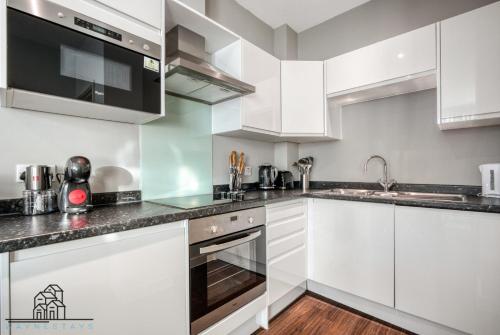 uma cozinha com armários brancos e electrodomésticos de aço inoxidável em Cosy 1-Bed by Heathrow Airport em Londres