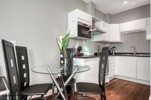 uma pequena cozinha com uma mesa de vidro e cadeiras em Cosy 1-Bed by Heathrow Airport em Londres