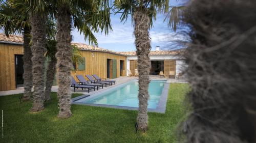 une villa avec une piscine entre deux palmiers dans l'établissement La villa Terracotta - Villa de rêve au calme à 900 m de l'océan avec piscine chauffée, à Sainte-Marie de Ré