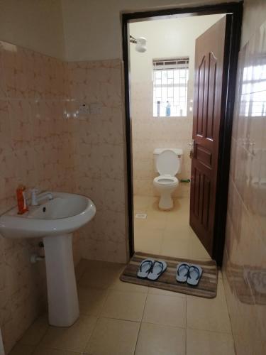 a bathroom with a sink toilet and a pair of slippers at Nash Issah Studio10 - 1bedroom in Nakuru