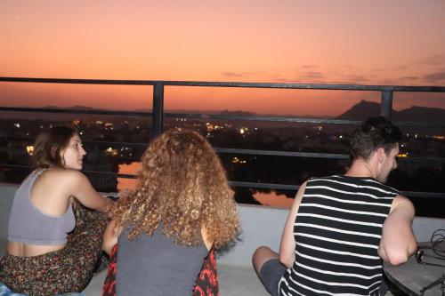 烏代浦的住宿－Bunkyard Hostel，三人组坐在阳台上欣赏日落