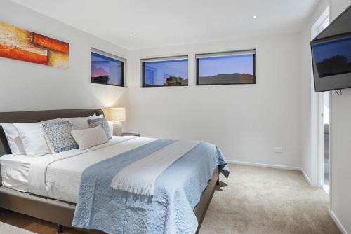 a white bedroom with a bed and three windows at Nexus Townhouse with Parking and Wi-Fi in Auckland