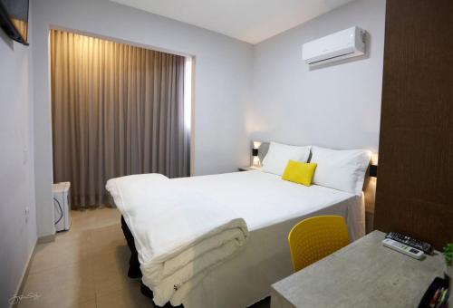 Aero Inn Hotel في أبرلانديا: غرفة بالفندق سرير ابيض ومخدة صفراء