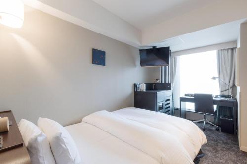 a bedroom with a white bed and a desk and a window at SHIROYAMA HOTEL kagoshima in Kagoshima