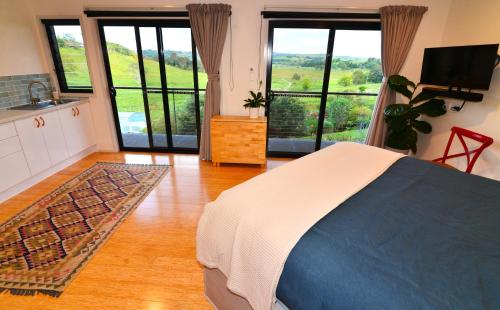 Studio with Rural views في Goonellabah: غرفة نوم بسرير ومطبخ بنوافذ كبيرة