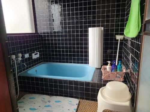 a blue tub in a black tiled bathroom at ゲストハウス陽だまりの宿 in Tomi