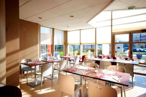 un restaurant avec des tables, des chaises et des fenêtres dans l'établissement Campanile Paris Ouest - Gennevilliers Barbanniers, à Gennevilliers