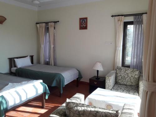 a bedroom with two beds and a chair and a window at Drala Resort Nepal in Kathmandu