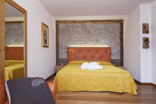 a bedroom with a bed with yellow sheets and a mirror at Alpenhotel Panorama in Campitello di Fassa