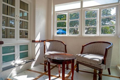 two chairs and a table in a room with windows at Citrus Chambers Mahabaleshwar in Mahabaleshwar
