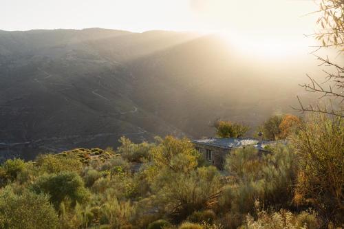 a house in the middle of a mountain with the sun setting at Cortijo La Vista in Órgiva