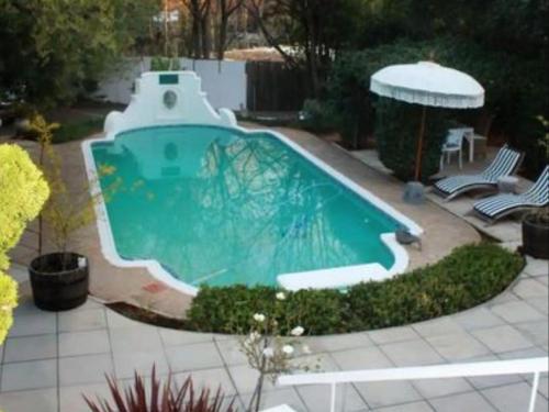 a swimming pool in a yard with two chairs and an umbrella at La Belle Guest House in Bloemfontein