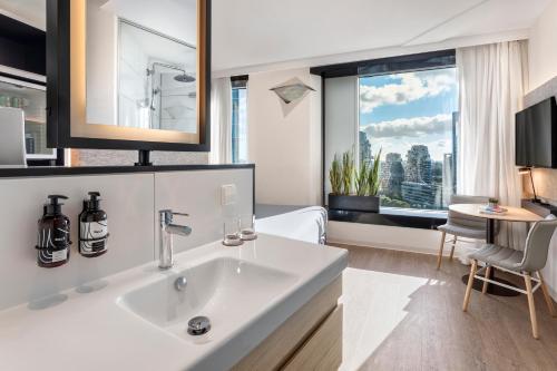 een badkamer met een wastafel en een slaapkamer met een raam bij INNSiDE by Meliá Amsterdam in Amsterdam