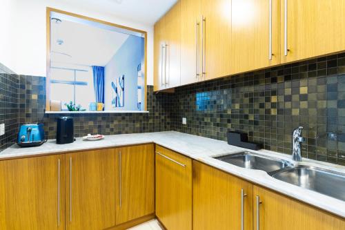 cocina con armarios de madera, fregadero y ventana en Vacay Lettings - Iris blue spectacular Marina view Apartment, en Dubái