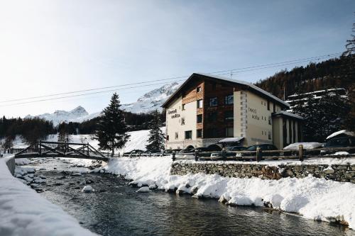 a building in the snow next to a river at Hotel Nolda in St. Moritz