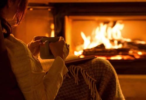 a woman sitting in front of a fireplace holding a book at Hill top view farm stay in Uruti