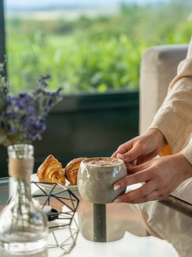 een persoon die een kopje vasthoudt op een tafel met gebakjes bij Apartahotel Suites Vila Birdie in Navata
