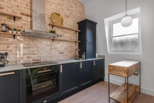 a kitchen with black cabinets and a brick wall at Central London-Modern Contemporary Flat in London