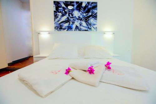 a white bed with white sheets and pink flowers on it at Nature Paradise Pool & Spa - Exceptional Secluded Luxury Location in Le Diamant