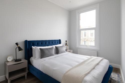 a white bedroom with a blue bed and a window at The Fulham Secret - Classy 5BDR Apartment in London