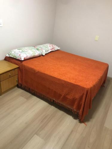 1 cama con colcha de color naranja y mesita de noche en Residencial Jardim Curitiba, en Curitiba