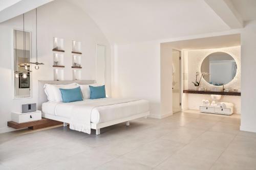 a white bedroom with a bed with blue pillows at Nikki Beach Resort & Spa Santorini in Kamari