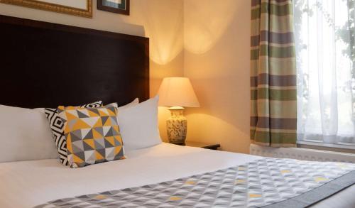 ein Schlafzimmer mit einem Bett, einer Lampe und einem Fenster in der Unterkunft The Welcombe Golf & Spa Hotel in Stratford-upon-Avon