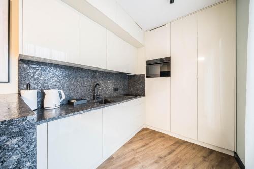 a kitchen with white cabinets and a wooden floor at Rent like home - Krysiewicza 3 in Poznań