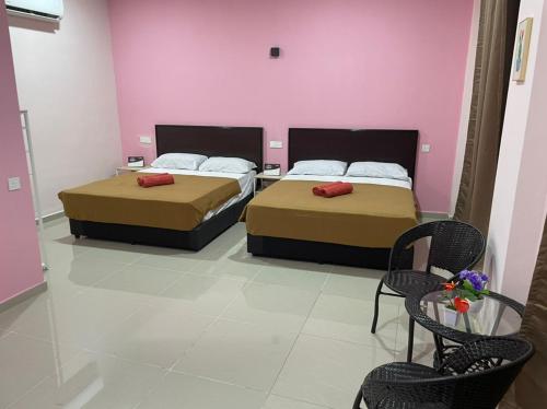 two beds in a room with two chairs and pink walls at A&H HOUSE HOTEL in Melaka