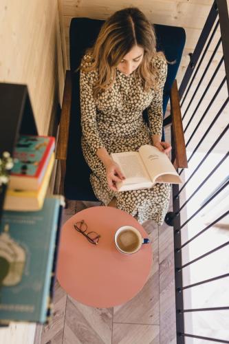 a woman sitting in a chair reading a book and a cup of coffee at LasHouse - Nowoczesna stodoła z widokiem na las in Bronków