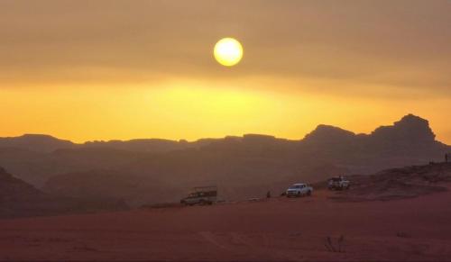 a sunset in the desert with cars parked in the sand at White Desert Camp in Wadi Rum