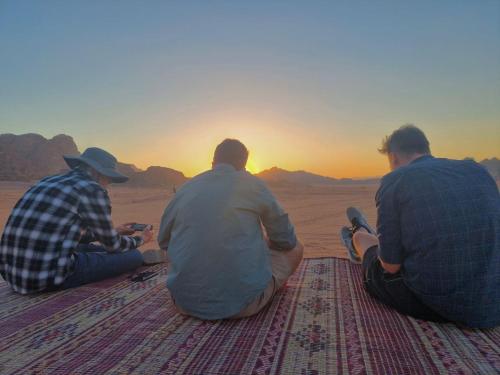three men sitting in the desert watching the sunset at White Desert Camp in Wadi Rum